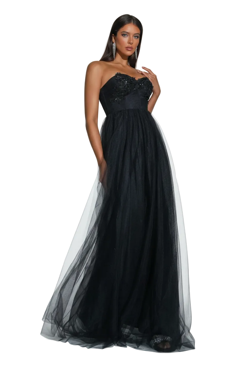 A woman modeling a strapless black formal gown with a heavily embellished sweetheart bodice and a voluminous tulle skirt, standing against a light gray studio backdrop. The Miss Ord logo is visible in the top left corner.