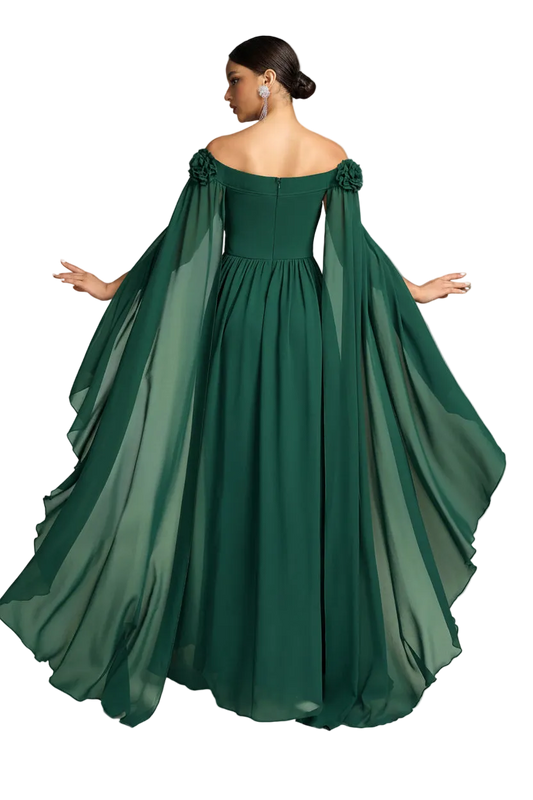 A woman modeling an off-the-shoulder floor-length gown in dark emerald green, shown from the back. The dress features a fitted bodice, a full skirt, and dramatic flowing cape-like sleeves with floral details at the shoulders, set against a plain white background.