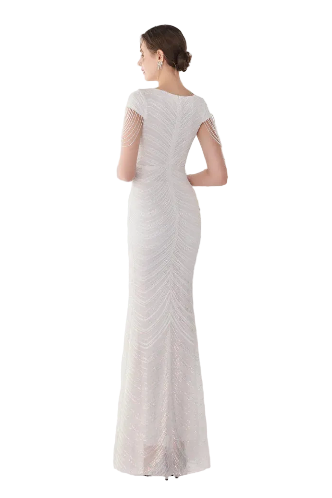 Woman in a white evening gown standing in front of a mirror in a minimalistic room.
