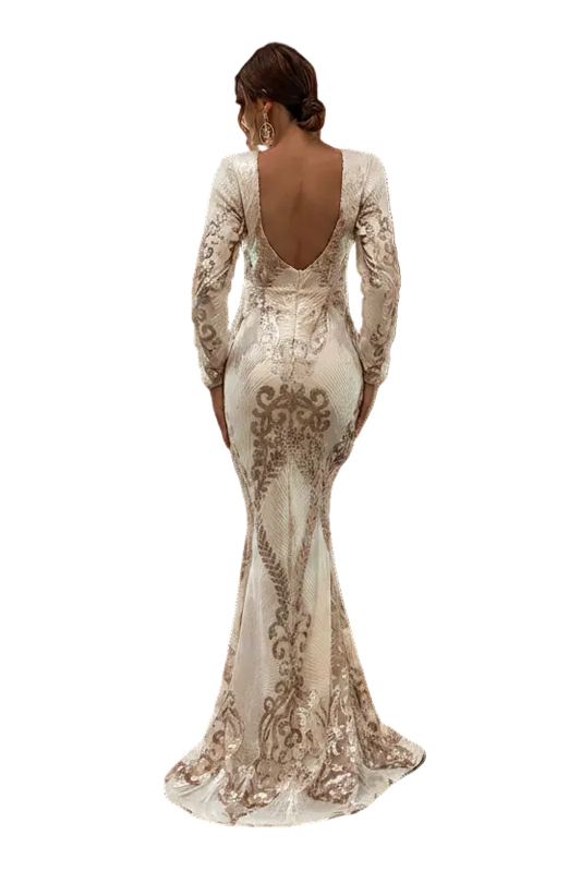 A woman stands in a white arched corridor wearing a fitted long-sleeve mermaid gown with a deep open back and ornate beige sequin embroidery over a light nude base.