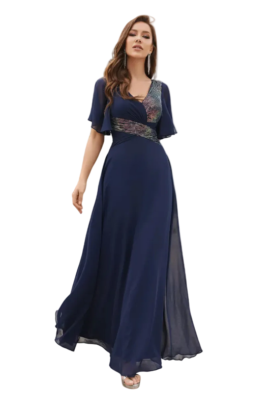 Woman in a long navy blue dress standing outdoors with palm trees and a pool in the background.