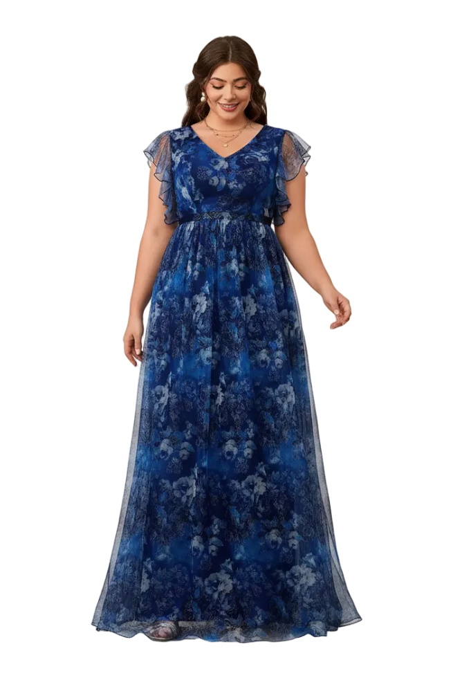 A woman modeling a floor-length blue floral gown with sheer flutter sleeves, standing in front of a peach-colored arched studio backdrop.