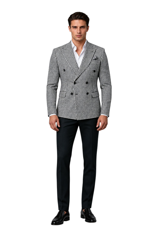 A man wearing a black and white houndstooth double-breasted blazer over a white dress shirt, standing against a textured gray studio background. A stylized 'UA' logo is visible in the top-left corner.