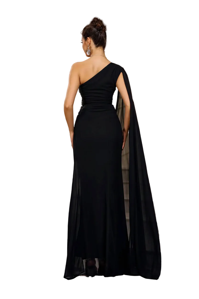 Woman in a black one-shoulder gown with a cape standing on a staircase.