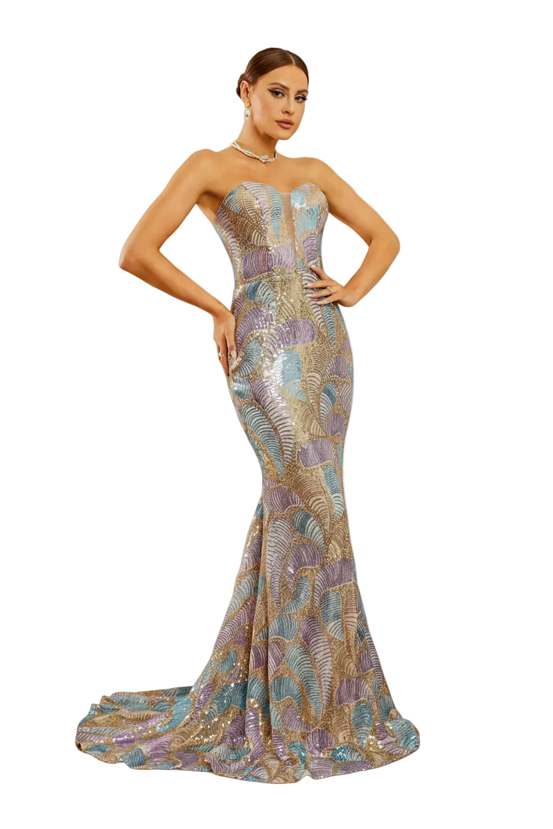 A woman models a strapless mermaid evening gown with a train, featuring an iridescent multicolor pattern of gold, purple, and blue. She is posed in front of an ornate white fireplace mantel in a decorated room.