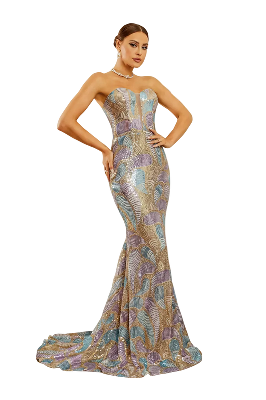 A woman models a strapless mermaid evening gown with a train, featuring an iridescent multicolor pattern of gold, purple, and blue. She is posed in front of an ornate white fireplace mantel in a decorated room.