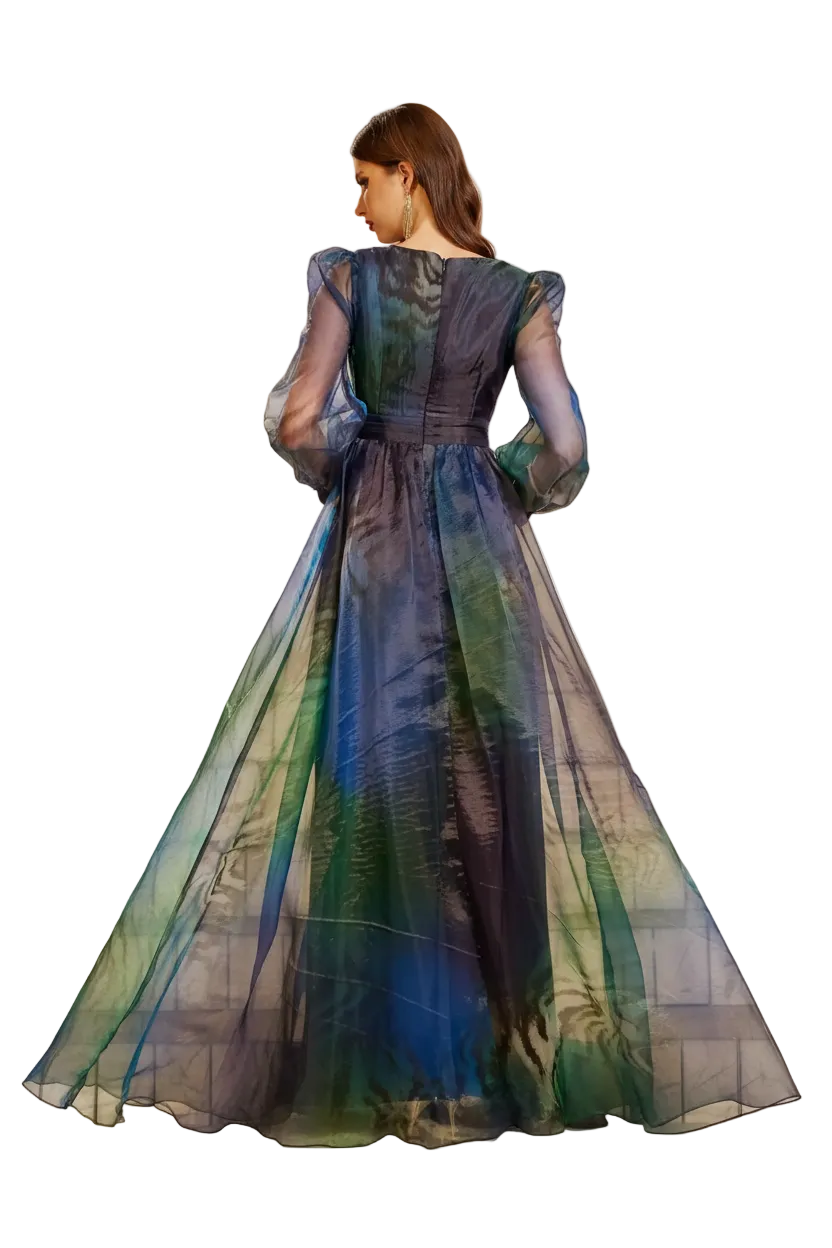A woman stands on stone stairs wearing a voluminous sheer evening gown with a dark blue, green, and teal abstract watercolor-like print. The dress features puffed long sleeves, a fitted waist, and a full flowing skirt.