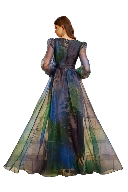 A woman stands on stone stairs wearing a voluminous sheer evening gown with a dark blue, green, and teal abstract watercolor-like print. The dress features puffed long sleeves, a fitted waist, and a full flowing skirt.