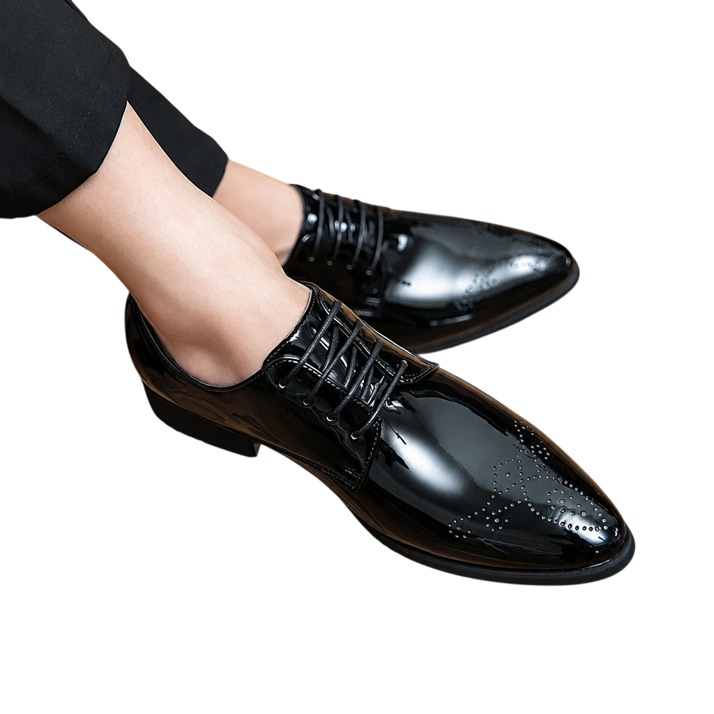 A pair of men's black leather oxford dress shoes with a glossy finish and subtle brogue detailing, shown on a person's feet against a wooden floor background.