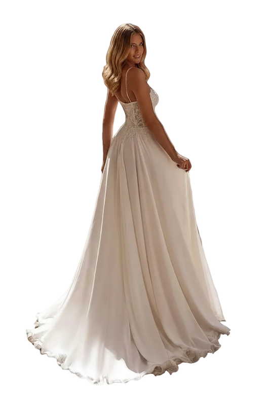 A woman wearing a white A-line wedding dress with a backless open back and lace bodice, photographed outdoors on a stone walkway near a building entrance. The dress has thin straps, a fitted bodice, and a full flowing skirt with a slight train.