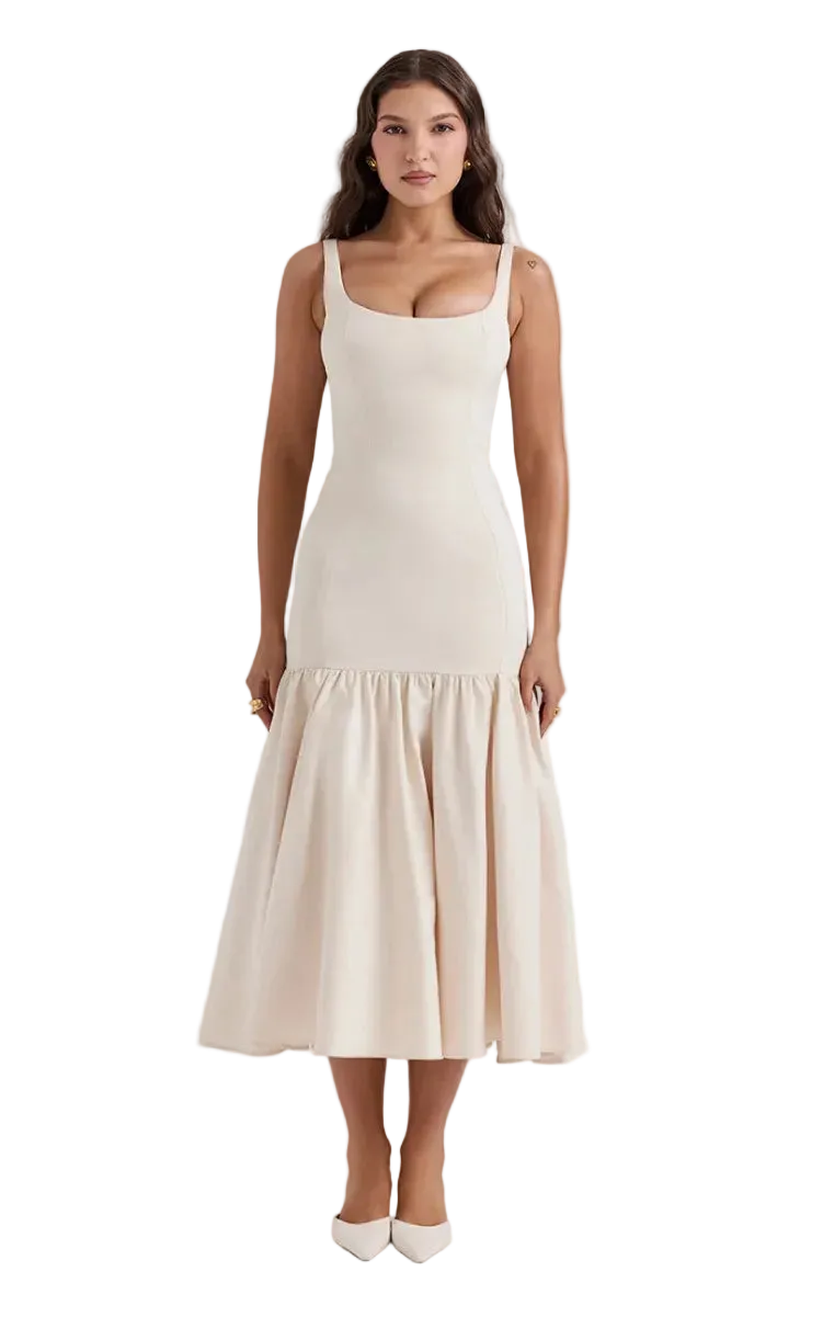 A woman modeling a sleeveless midi dress with a square neckline, thin shoulder straps, a fitted bodice, and a flared ruffled hem. The dress is a warm off-white/cream color, paired with matching pointed-toe heels, set against a plain white studio background.