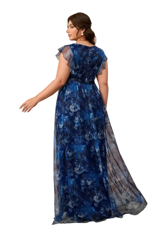 A woman modeling a floor-length blue floral gown with sheer cap sleeves and a sheer side panel, photographed in a studio with warm beige arched walls.