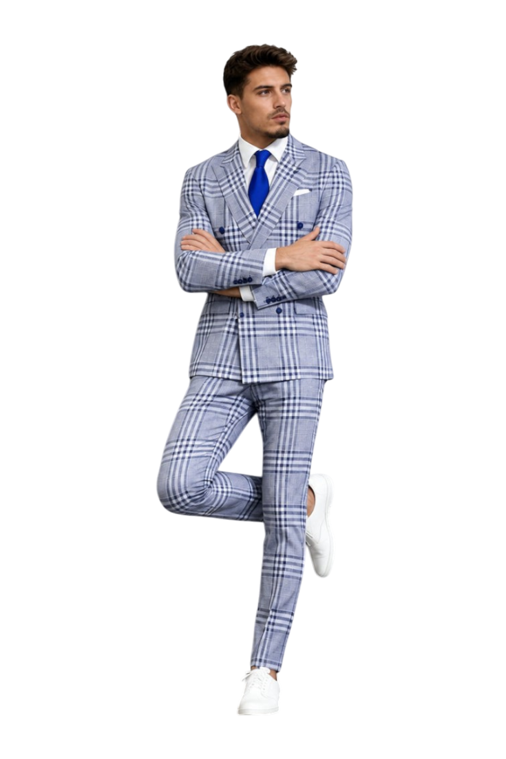 A man models a light blue and white plaid three-piece suit with a white shirt, blue tie, and white sneakers, posing against a textured gray wall. The brand logo 'UA' is visible in the top left corner.