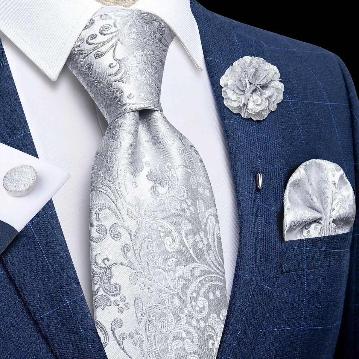 JASE HEART GLOBAL silver paisley necktie set with matching pocket square, lapel flower, and cufflinks on a blue suit.